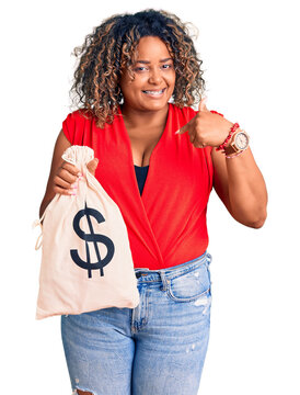 Young african american plus size woman holding money bag with dollar symbol pointing finger to one self smiling happy and proud