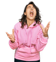 Young hispanic woman wearing casual sweatshirt celebrating mad and crazy for success with arms...