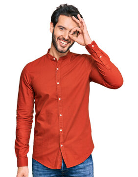 Young hispanic man wearing casual clothes doing ok gesture with hand smiling, eye looking through fingers with happy face.