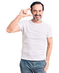 Middle age handsome man wearing casual t-shirt smiling and confident gesturing with hand doing small size sign with fingers looking and the camera. measure concept.