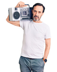 Middle age handsome man listening to music using vintage boombox thinking attitude and sober expression looking self confident