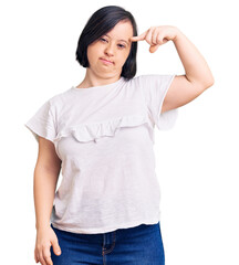 Fototapeta premium Brunette woman with down syndrome wearing casual white tshirt pointing unhappy to pimple on forehead, ugly infection of blackhead. acne and skin problem