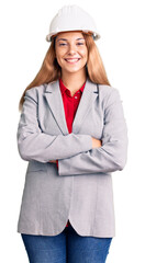 Beautiful young woman wearing architect hardhat happy face smiling with crossed arms looking at the camera. positive person.