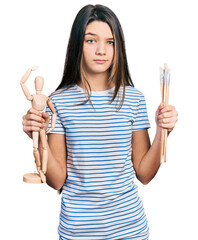 Young brunette girl with long hair holding small wooden manikin and pencils skeptic and nervous, frowning upset because of problem. negative person.