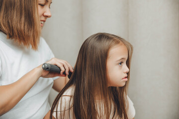 Fototapeta premium a little dark-haired girl looks into the camera and smiles while her mother combs her daughter's hair. hair care