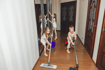 The concept of cleaning an apartment on the weekend. Mom and her children are cleaning the house, Woman and little children are sweeping, vacuuming the floor, dancing