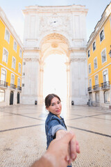 Fototapeta na wymiar Travel vacation couple - Woman walking on romantic honeymoon vacation in Lisbon hand in hand with her boyfriend following her, view from behind. POV.
