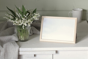 an empty frame and lilies of the valley. Cottage interior. background, copy space. summer stage creator.