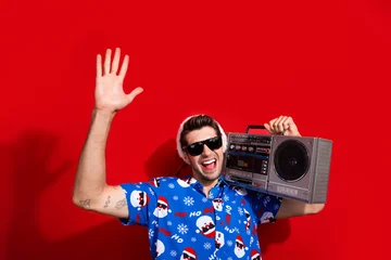 Deurstickers Portrait of young guy student raised palm up clubber carry tape player boombox welcome to christmas party isolated on red color background © deagreez