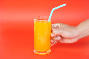 Close up of man hand holding glass of orange juice with drinking straw, on red background. Concept, morning refreshing beverage. Sweet, testy and high vitamin C.                     - obrazy, fototapety, plakaty