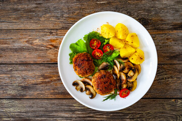 Fried pork meatballs with boiled potatoes and fried mushrooms on wooden table

