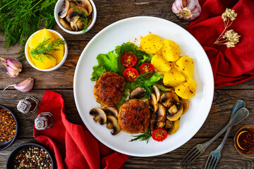 Fried pork meatballs with boiled potatoes and fried mushrooms on wooden table
