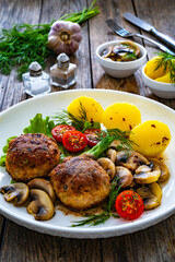Fried pork meatballs with boiled potatoes and fried mushrooms on wooden table

