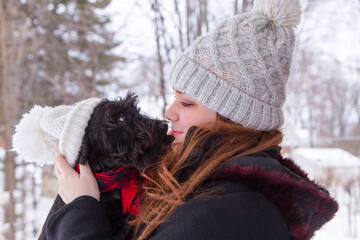 Medium shot of cute red-haired young woman in winter clothes holding her miniature black Schnauzer...