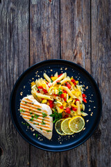 Grilled chicken breast with penne noodles, lemon and pepper on wooden background
