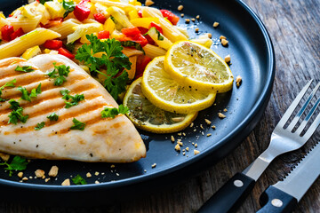 Grilled chicken breast with penne noodles, lemon and pepper on wooden background
