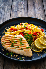 Grilled chicken breast with penne noodles, lemon and pepper on wooden background
