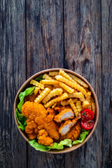 Fried breaded chicken nuggets served with French fries and vegetables on wooden table
