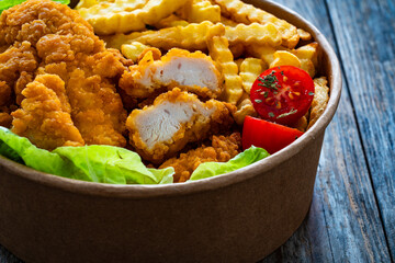 Fried breaded chicken nuggets served with French fries and vegetables on wooden table
