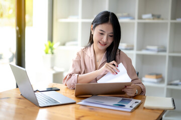 Fototapeta premium Asian businesswoman sitting and working check documents analyze market reports. Review and compare report data.