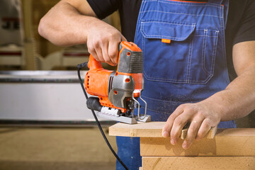 A carpenter using a jigsaw to cut wood cuts bars. Home repair concepts, close up.