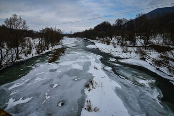 Fototapeta premium Mountain village in the Ukrainian Carpathians next to the river, winter landscape