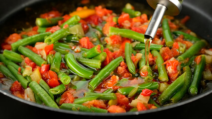 Pouring oil for frying vegetables in pan. Green beans, tomatoes, bell peppers ready for cooking