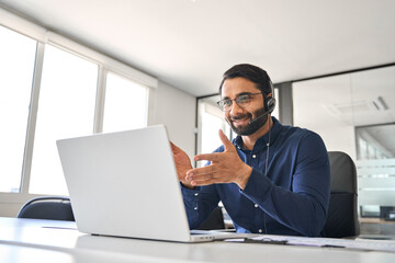 Busy Indian call center agent wearing headset talking to client working in customer support office. Professional contract service operator telemarketing representative using laptop having conversation