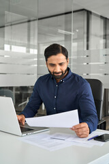 Busy Indian business man holding project document report checking financial results analyzing...