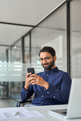 Professional Indian business man working using smartphone in office. Vertical shot. Smiling company...