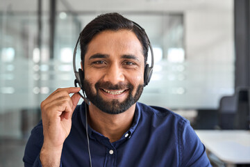 Happy Indian man call center agent wearing headset in office. Smiling male contract service representative telemarketing operator looking to camera working in customer support. Headshot portrait.
