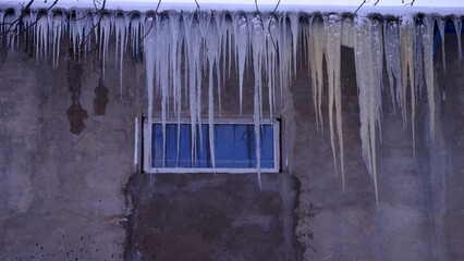 Many large icicles hang from the roof of the old building.