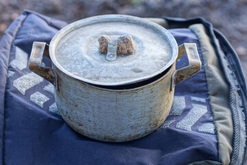 one old dirty closed aluminum pan standing on a black cloth on a table on the street