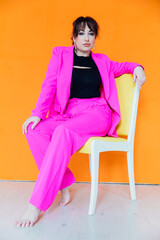 Woman in suit posing on a chair on an orange background