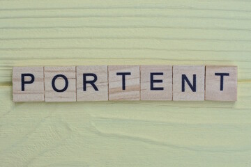 the word portent of gray small wooden letters lies on a yellow wooden table
