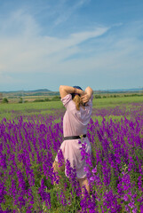 A girl in spring flowers in a field in nature poses for a blog. Purple field of Delphínium flowers