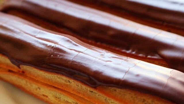French pastry eclairs with cream filling covered with melted milk chocolate circle rotation close up
