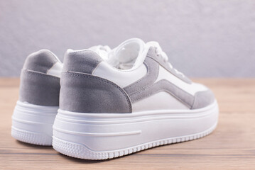 Naklejka premium White sports sneakers on a wooden background. Footwear