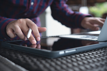 Casual business man using digital tablet, touching on screen and working on laptop computer, surfing the internet at coffee shop, close up. Man freelancer online working from cafe