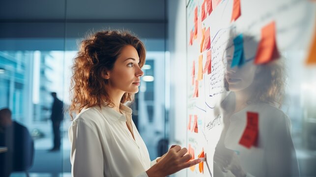 Focused businesswoman reads information on a notepad attached to a whiteboard and efficiently adds more details, showcasing her commitment to thorough information processing and organization.