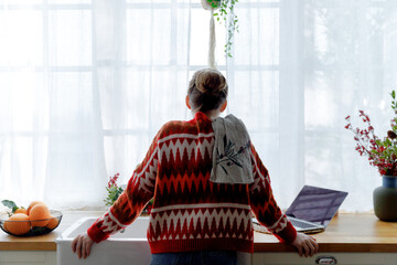 young woman in red sweater stays in kitchen leaning on sink feeling upset. thoughtful and...