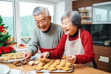 Happy elderly Asian couple cooks gingerbread men for Christmas holiday at home. Happy man and woman enjoy baking snacks for grandchildren. Cheerful grandparents make biscuits in kitchen - obrazy, fototapety, plakaty