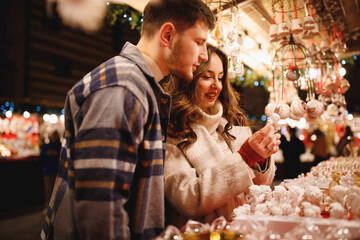 Young stylish couple in love in checkered coats choosing the Christmas toys at Christmas Verona...