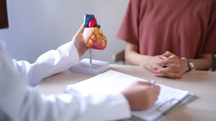 Asian cardiologist doctor women pointing on document and anatomical of heart model to explaining...