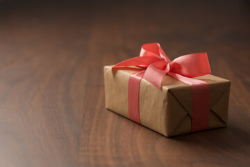 Obraz na płótnie Canvas Brown paper gift box with rose ribbon on walnut wood table with copy space