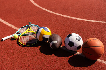 A variety of sports equipment including an american football, a soccer ball, a tennis racket, a tennis ball, and a basketball