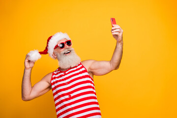 Photo of cool positive senior guy christmas swimwear hat glasses recording video vlog gadget empty space isolated yellow color background