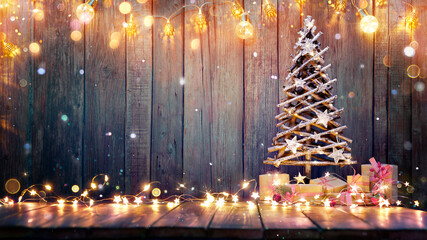 Christmas Decoration - Wooden Tree On Table With Rustic Lights And Abstract Defocused Snowing