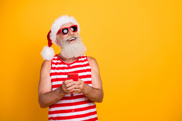 Photo of positive dreamy senior guy christmas swimwear hat glasses typing modern device empty space...