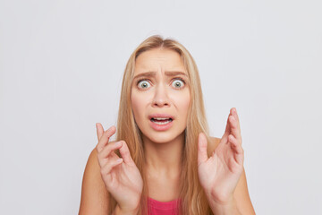 Portrait shot of scared blonde girl over white studio backdrop, eyes and mouth open, hands up, hard times concept, copy space